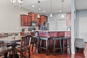A modern kitchen with wooden cabinets, a central island with stools, and a dining area with a round table and chairs.