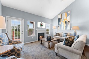 A living room with a fireplace, two sofas, a coffee table, and a television mounted on the wall.