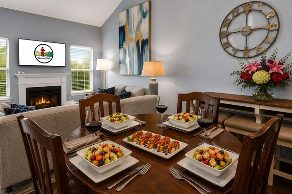 A dining room with a table set for a meal, a fireplace, and a clock on the wall.