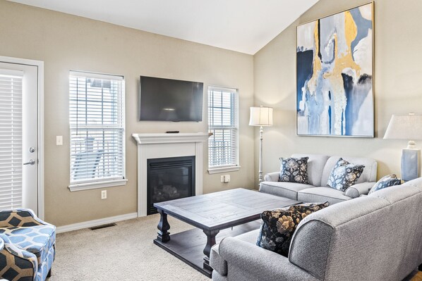 A living room with a fireplace, a sofa, a coffee table, and a TV mounted on the wall.