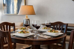 Una mesa de comedor con cuatro ensaladas y tres copas de vino tinto, rodeada de sillas de madera.