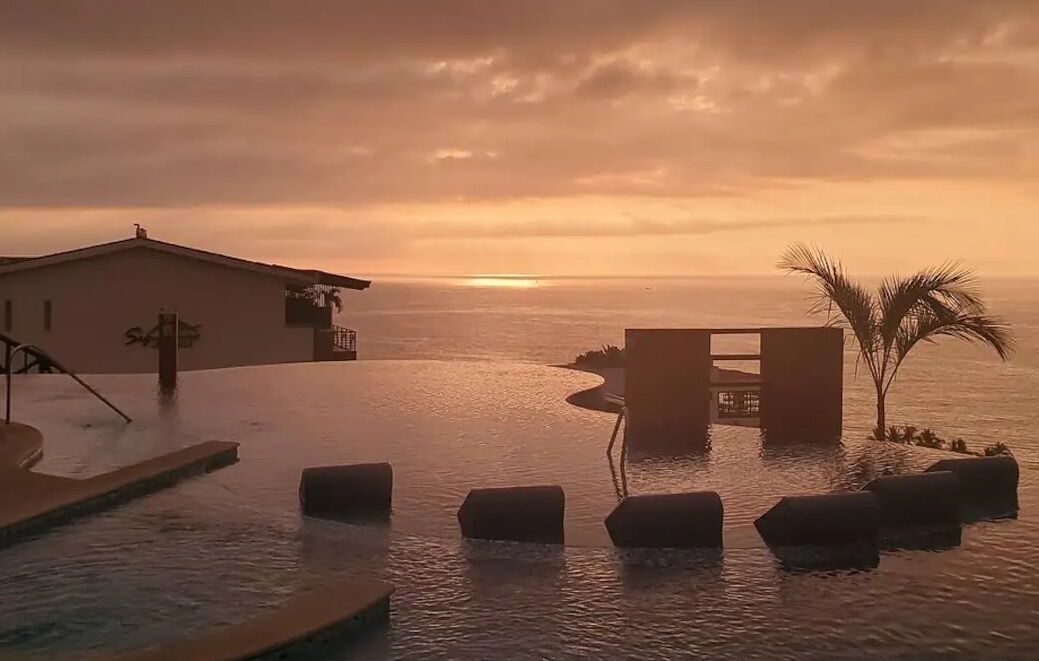A pool area with a sunset view, a building with a sign, and palm trees.