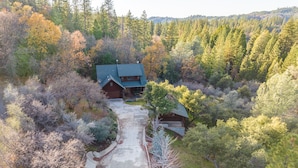 Una casa gran de dos pisos amb un porxo ben visible i un garatge, envoltada de bosc dens i turons.