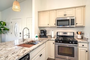 A kitchen with white cabinets, a stainless steel microwave, a gas stove, and a sink.