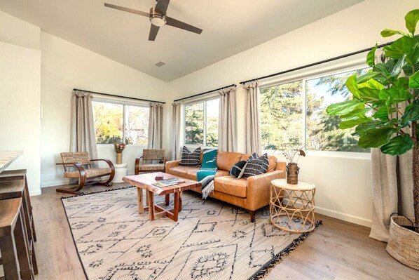 A spacious living room with a sofa, chairs, a coffee table, and a large window with curtains.