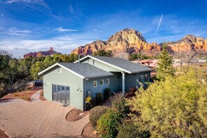 A two-story house with a garage, surrounded by trees and a mountain backdrop.