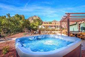 A hot tub in a backyard with a pergola, patio furniture, and a view of a mountain.