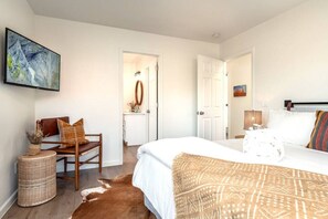 A bedroom with a large bed, a chair, a small table, and a painting on the wall.