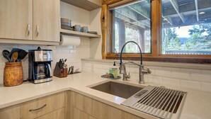 Una cocina con armarios de madera, una cafetera de acero inoxidable y una ventana con vista a árboles.