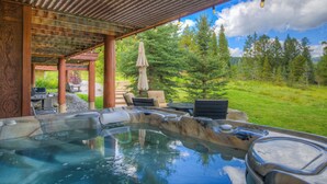 Un área de hidromasaje con un pérgola de madera, mobiliario exterior y vistas a un paisaje boscoso.