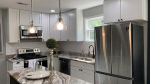 A modern kitchen with white cabinets, stainless steel appliances, a marble countertop, and pendant lighting. - Charming 3-Bed/1-Bath Home in Hyattsville, MD! (Hyattsville)