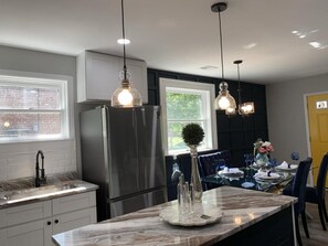 A modern kitchen with a marble countertop, stainless steel appliances, pendant lighting, and a dining area with a table set for four. - Charming 3-Bed/1-Bath Home in Hyattsville, MD! (Hyattsville)