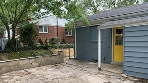 A stone patio area with a garden, a small shed, and a yellow door. - Charming 3-Bed/1-Bath Home in Hyattsville, MD! (Hyattsville)