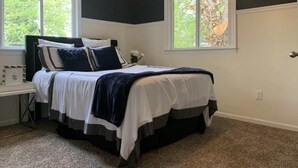 A bedroom with a bed, two windows, a nightstand, and a carpeted floor. - Charming 3-Bed/1-Bath Home in Hyattsville, MD! (Hyattsville)