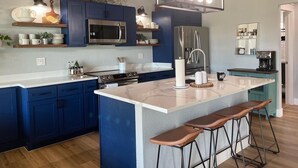 Una cocina moderna con gabinetes azules, electrodomésticos de acero inoxidable y una isla central con taburetes de bar.