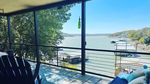 Un balcón con vista a un río y un muelle, una silla y una cama con almohadones.