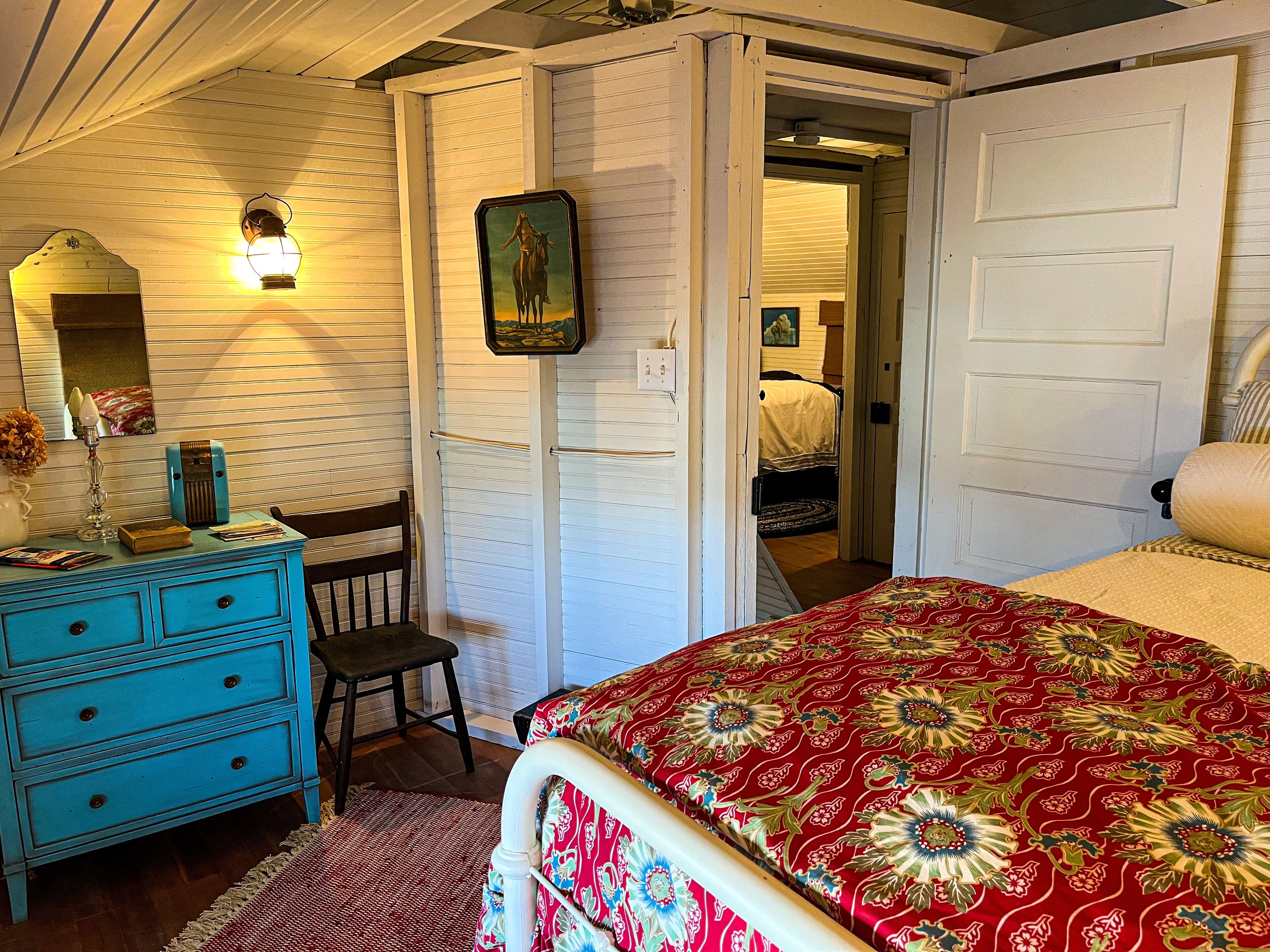 A bedroom with a bed, a dresser, a chair, and a door leading to another room.