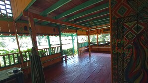 A wooden deck with a hammock, benches, and a view of greenery.