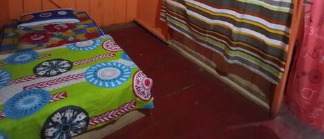 Ein Zimmer mit einem Bett, das mit einem farbenfrohen Blumendecken überzogen ist, einer orangefarbenen Wand, einem gestreiften Vorhang und einem weißen Vorhang, der am oberen Rand gebunden ist.