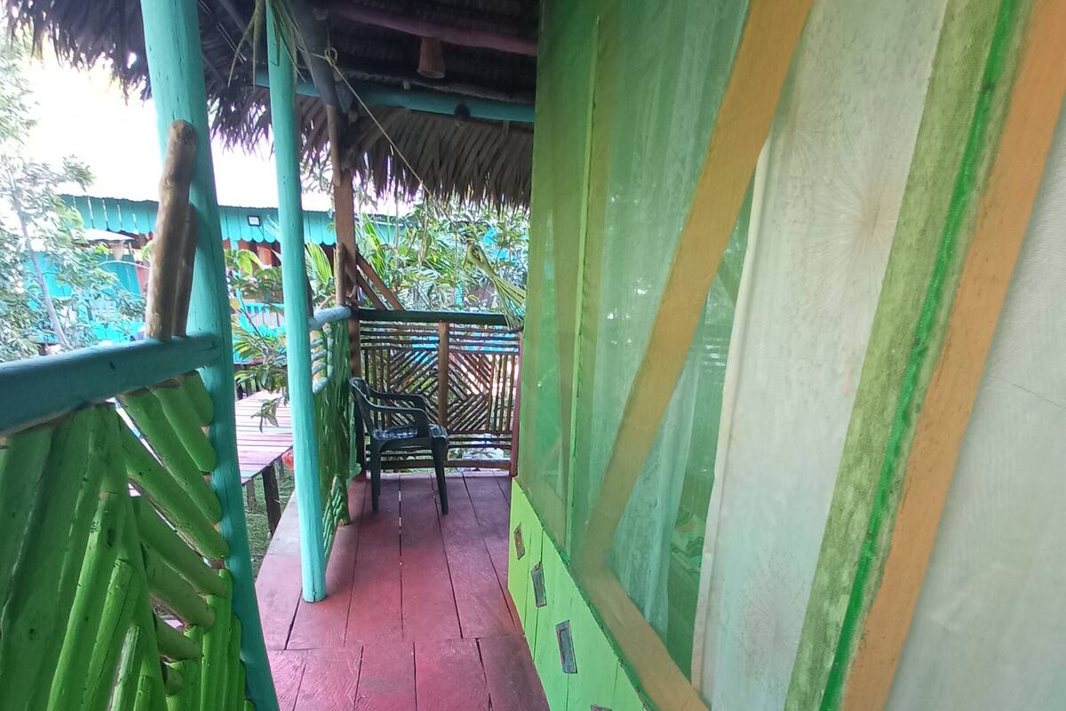 A covered walkway with a red floor, green railings, and a thatched roof.