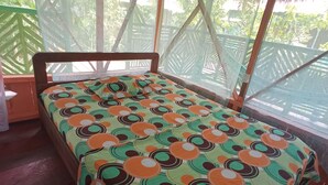 A bed with a colorful circular pattern bedspread in a room with a wooden headboard and a window with a mesh screen.
