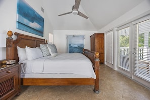 A bedroom with a wooden bed, a ceiling fan, a painting of the ocean, and a view of the outdoors through the door. - Private Pool Oasis - Centrally Located in Florida Keys (Duck Key)