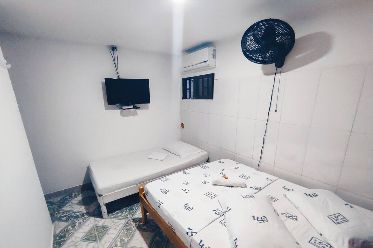 Una habitación pequeña con cama individual, televisión, aire acondicionado y ventilador.