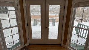 A room with a double door leading outside, a wooden floor, and a view of a snowy outdoor area with a fence and trees. - Your adventure home base for skiing, snowboarding, hiking and biking! (Ironwood)