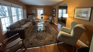 A living room with a sofa, armchairs, a coffee table, and a rug. There are two windows with curtains, a lamp, and a framed picture on the wall. - Your adventure home base for skiing, snowboarding, hiking and biking! (Ironwood)