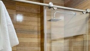Een douche met een glazen deur, houten lambrisering aan de wanden, en een handdoek hangend aan de linkerkant.
