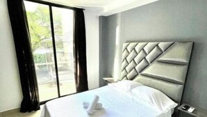 Een moderne hotelkamer met een groot bed, een hoofdeinde met een geometrisch patroon, een nachtkastje en een uitzicht door een groot raam.