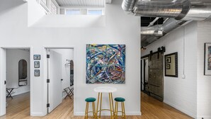 Una galería amplia con un gran cuadro abstracto, piso de madera y pared de ladrillo blanco.
