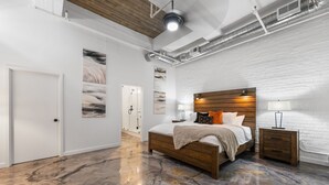 Un dormitorio con cama de madera, paredes de ladrillo blanco y suelo de mármol pulido.