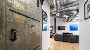 Un interior con piso de madera, un sofá gris, un televisor montado en la pared y un amplio ventanal con vistas al cielo.