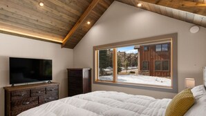 Ein Schlafzimmer mit einem großen Bett, einem Fernseher auf einer Holzkommode und einem Fenster mit Blick auf eine verschneite Landschaft.