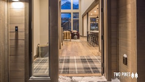 Un couloir intérieur aux murs en bois, agrémenté d’un tapis à carreaux, d’un coin bar et offrant une vue sur un paysage enneigé grâce à de grandes fenêtres.