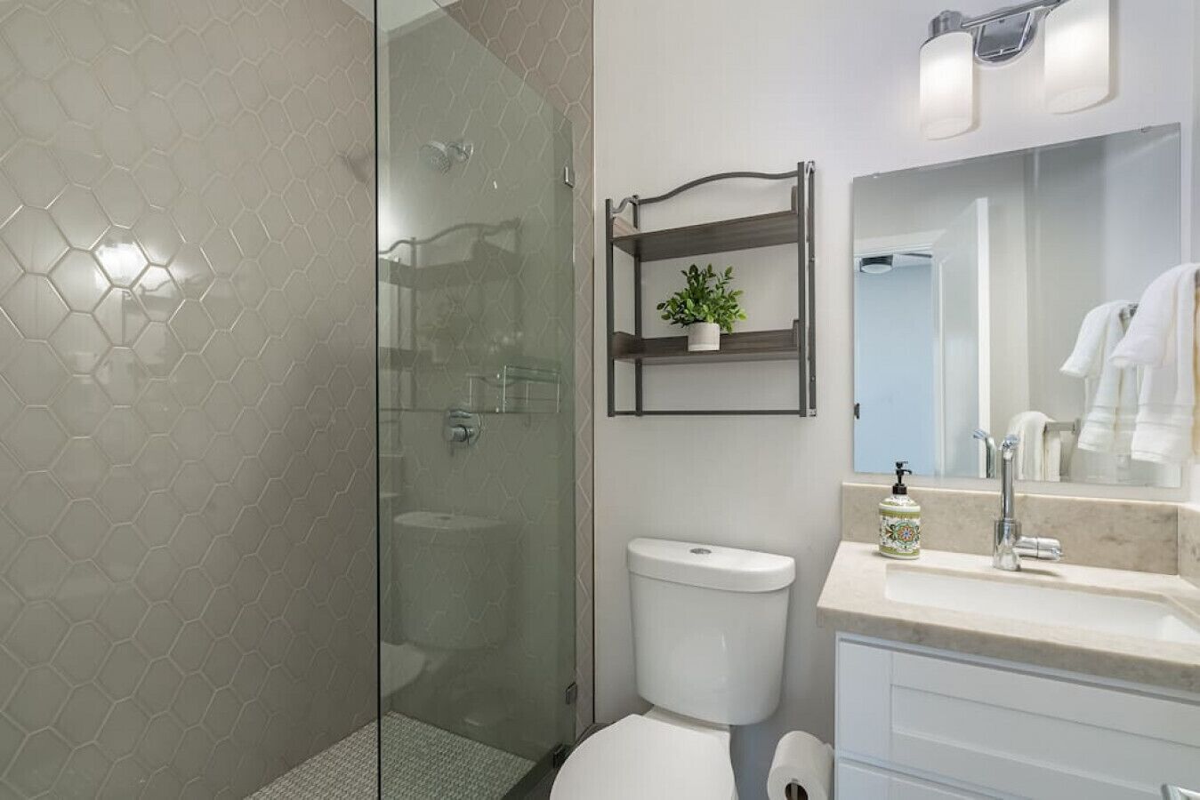 A modern bathroom with a glass shower enclosure, a white toilet, a sink with a mirror, and a shelf with a plant.