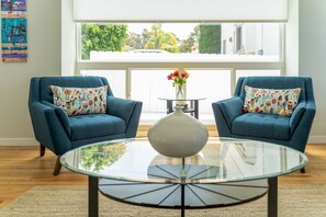 A modern living room with two blue armchairs, a glass coffee table, and a vase with flowers.