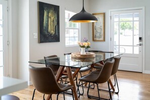 A modern dining area with a glass table, leather chairs, and a black pendant light.