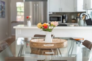 Une cuisine moderne avec une table à manger en verre, un vase blanc orné de fleurs et des appareils électroménagers en acier inoxydable.