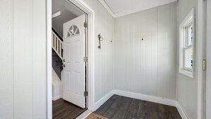 Un couloir aux murs blancs, avec un plancher en bois, une porte blanche et une fenêtre.