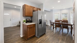 Une cuisine moderne avec des meubles en bois, un réfrigérateur en acier inoxydable, un appareil à café intégré et un coin repas avec des chaises et une table en bois.