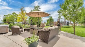 An outdoor patio area with wicker furniture, a large umbrella, and a hot tub. - The Suite at the Cedars (Cedar Hills)
