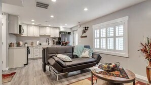 A modern kitchen with white cabinets, a black leather sofa, and a dining table with a floral table runner. - The Suite at the Cedars (Cedar Hills)