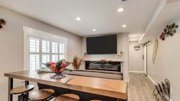 A modern kitchen with a central island, bar stools, a large window, and a flat-screen TV mounted above the island. - The Suite at the Cedars (Cedar Hills)