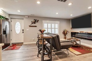 A modern kitchen with a built-in refrigerator, a dining area with a table and chairs, a large window, and a flat-screen TV mounted on the wall.