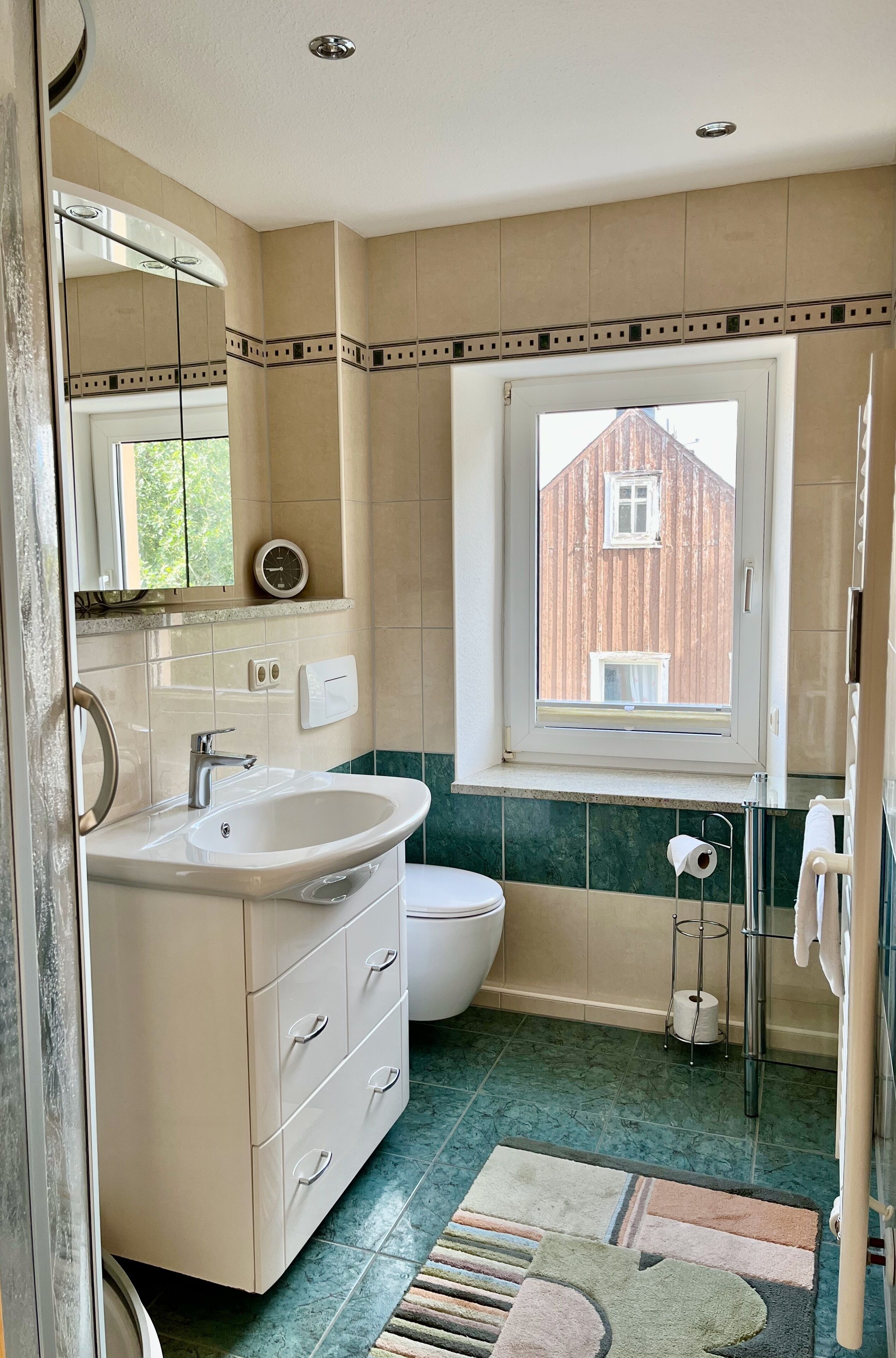 Un baño con lavamanos, inodoro y ventana con vista a un edificio de madera.