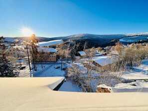 A snow-covered landscape with a building that appears to be a hotel or guesthouse, surrounded by trees and a clear sky. - Landhaus-Chalet-Keilberger Blick  (Oberwiesenthal)