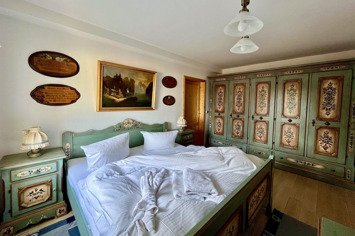 Un dormitorio con cama, cómoda, mesita de noche, lámpara y un cuadro en la pared.