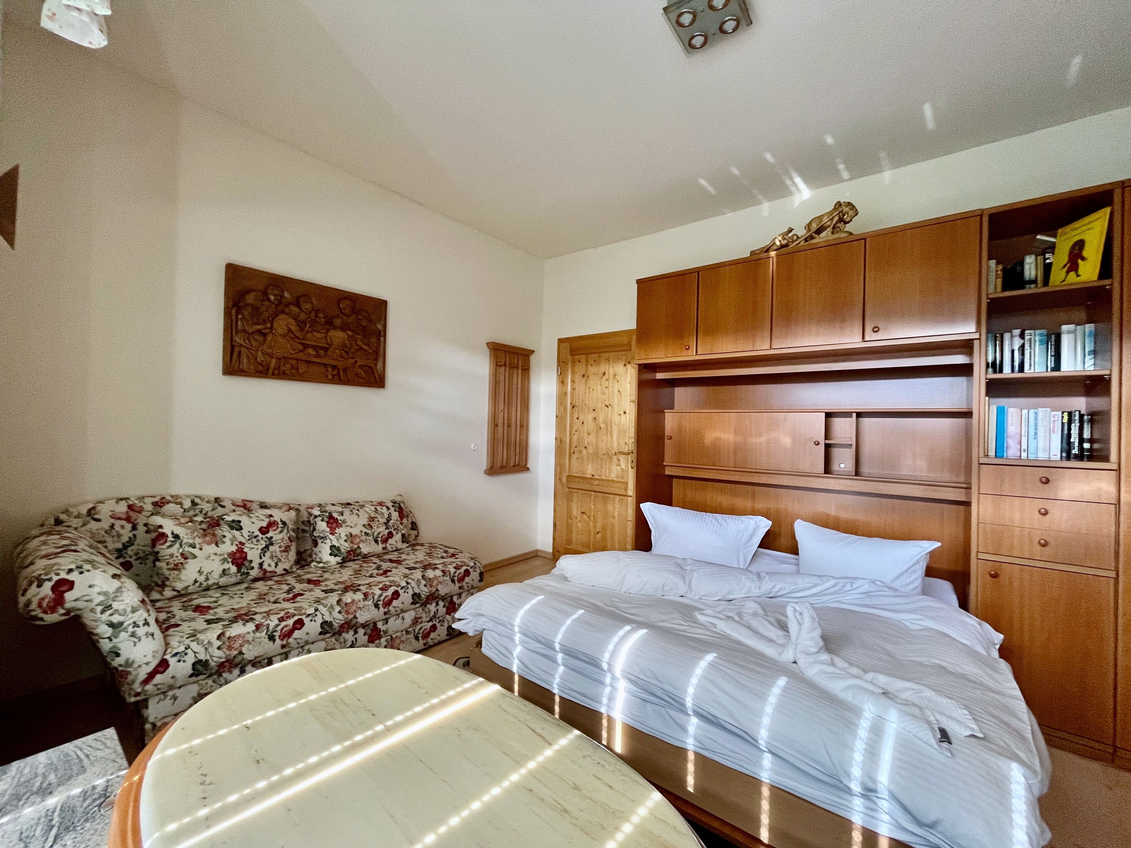 Un dormitorio con una cama, un armario de madera, un sofá floral y un cuadro en la pared.